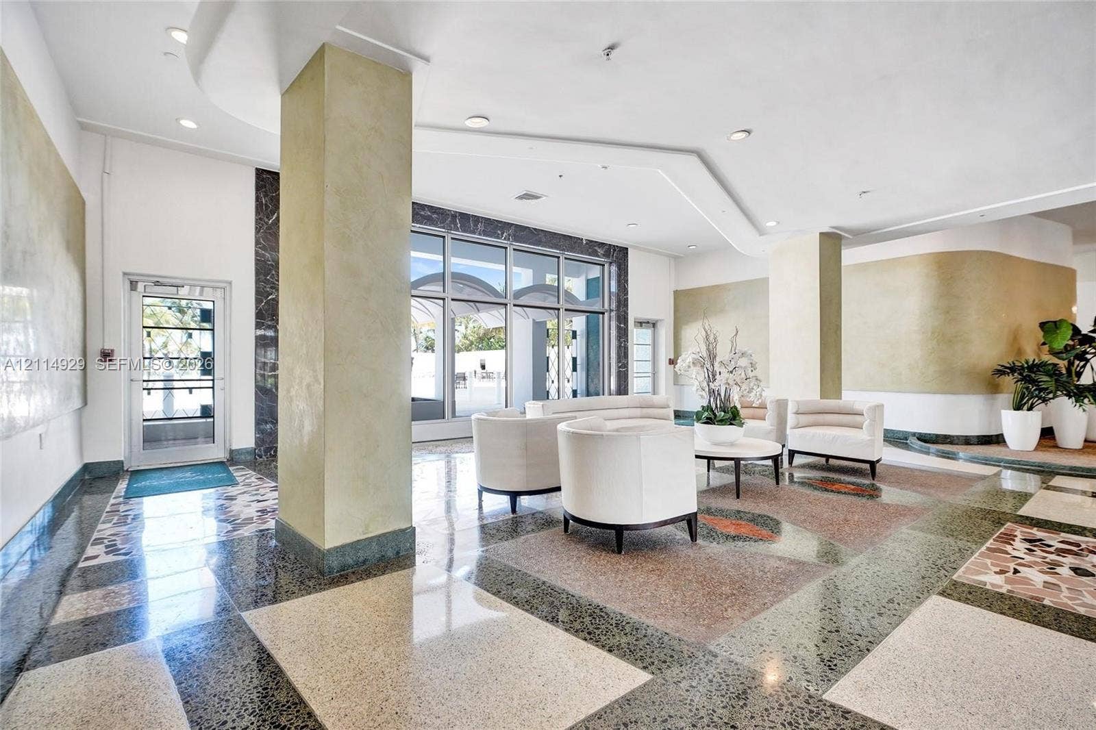 Grand lobby featuring geometric terrazzo flooring, floor-to-ceiling glass paneling, recessed tray ceilings, and textured wall finishes