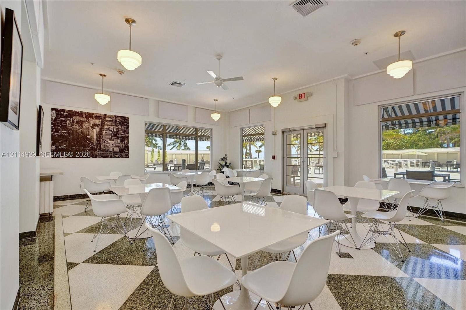 Large open-concept space featuring geometric patterned flooring, expansive glass windows with exterior awnings, recessed lighting, and multiple pendant fixtures