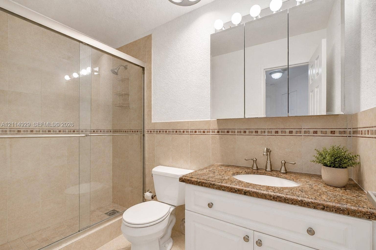 Bathroom featuring a vanity with a stone countertop, an integrated oval sink, a tri-panel mirrored medicine cabinet, and a tiled shower enclosure with a glass door