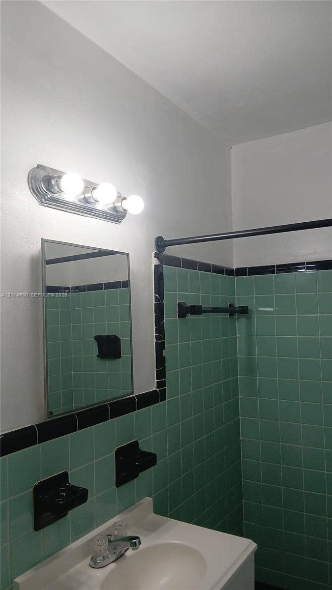 319 NE 2nd Street, #1, Hallandale Beach, Hallandale Beach, FL 33009 Wall-mounted three-bulb chrome light fixture, rectangular medicine cabinet, integrated sink vanity, and custom green wall tile with black trim accents