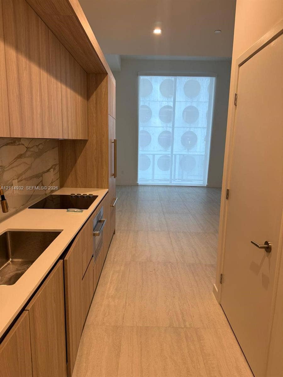 77 SE 5th Street, #607, Miami, FL 33141 Kitchen featuring wood-finish cabinetry, stone-surface countertops, full-height decorative backsplash, stainless steel sink, and large-format tile flooring