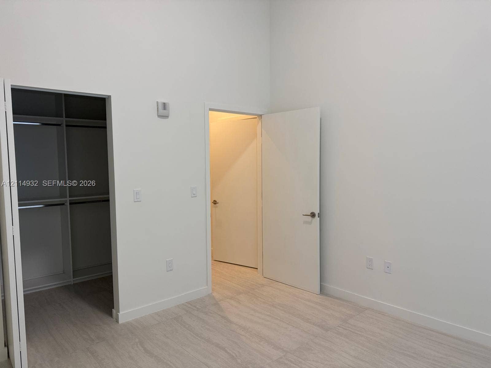77 SE 5th Street, #607, Miami, FL 33141 High-ceilinged room featuring light-toned wood-finish flooring, white walls, built-in closet shelving, and solid-core doors with brushed-metal hardware
