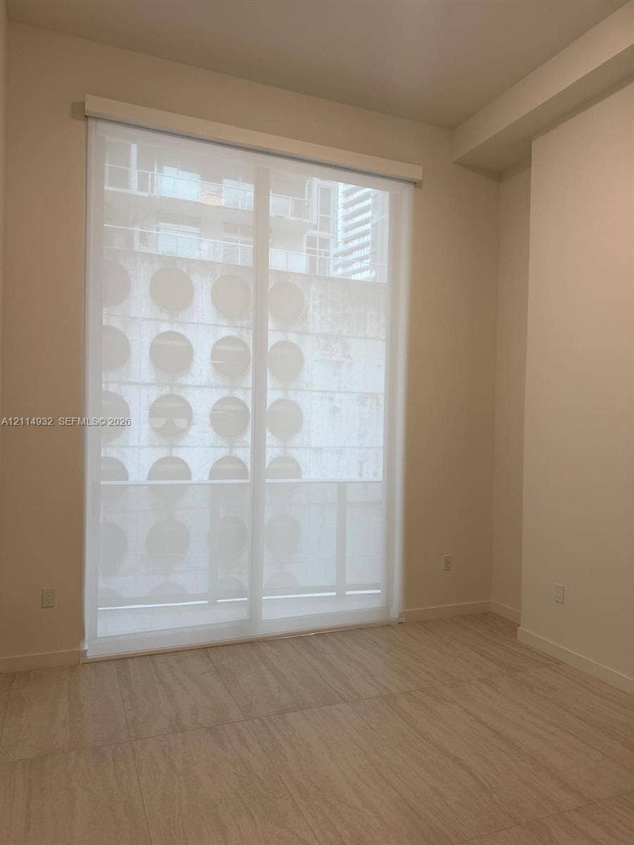 77 SE 5th Street, #607, Miami, FL 33141 Floor-to-ceiling glass sliding door with white roller shade, neutral tile flooring, and smooth-finish walls