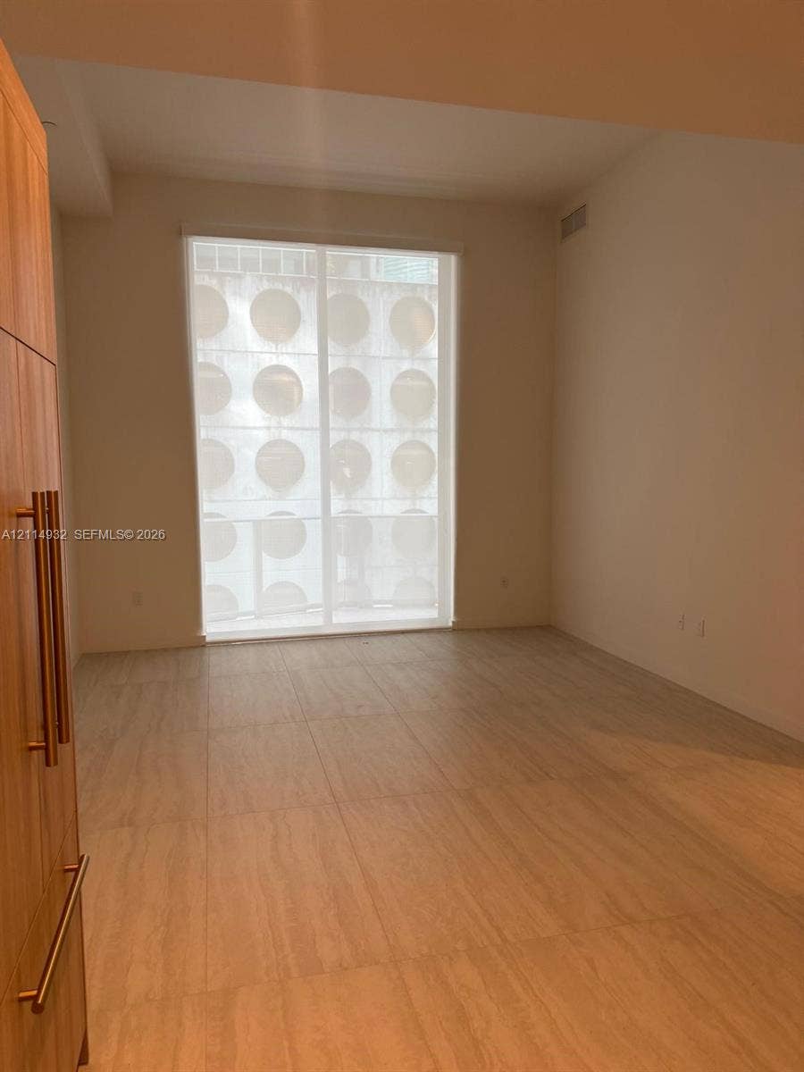 77 SE 5th Street, #607, Miami, FL 33141 Large-format tile flooring, floor-to-ceiling window with privacy screen, and built-in wood-finish cabinetry featuring vertical bar pulls