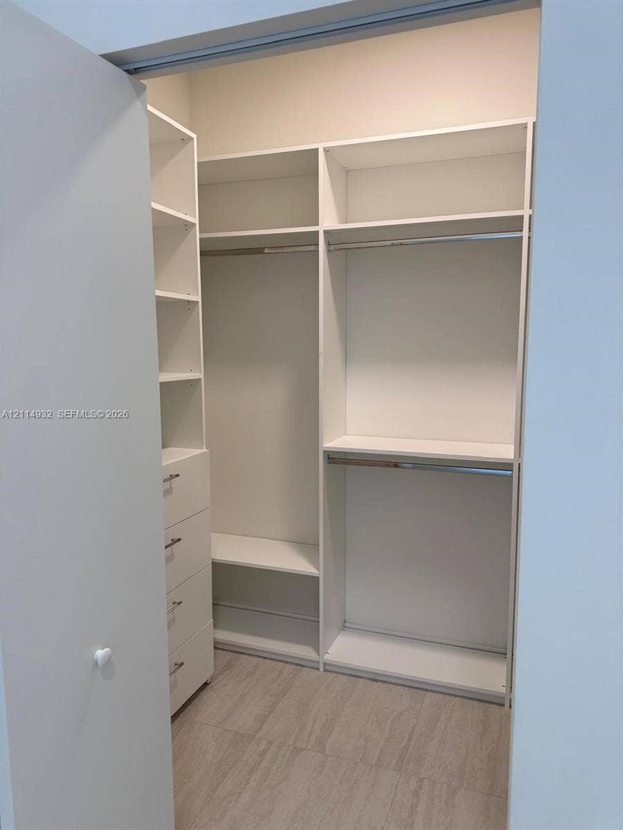 77 SE 5th Street, #607, Miami, FL 33141 Custom storage system featuring white built-in cabinetry, multiple adjustable shelves, integrated hanging rods, and a four-drawer stack with metallic hardware, finished with wood-finish flooring