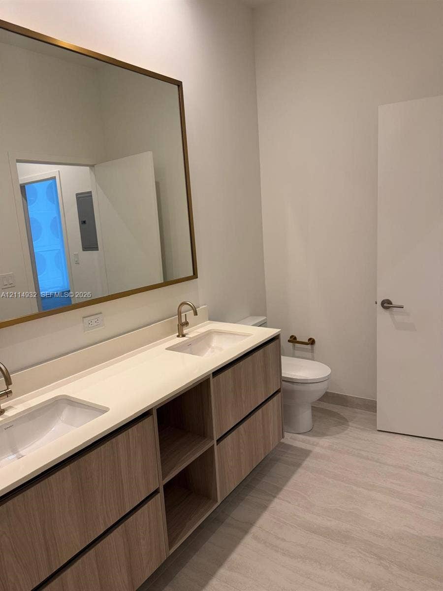 77 SE 5th Street, #607, Miami, FL 33141 Floating wood-finish vanity with a double-basin countertop, undermount sinks, brass-toned fixtures, and a large rectangular mirror with a matching frame