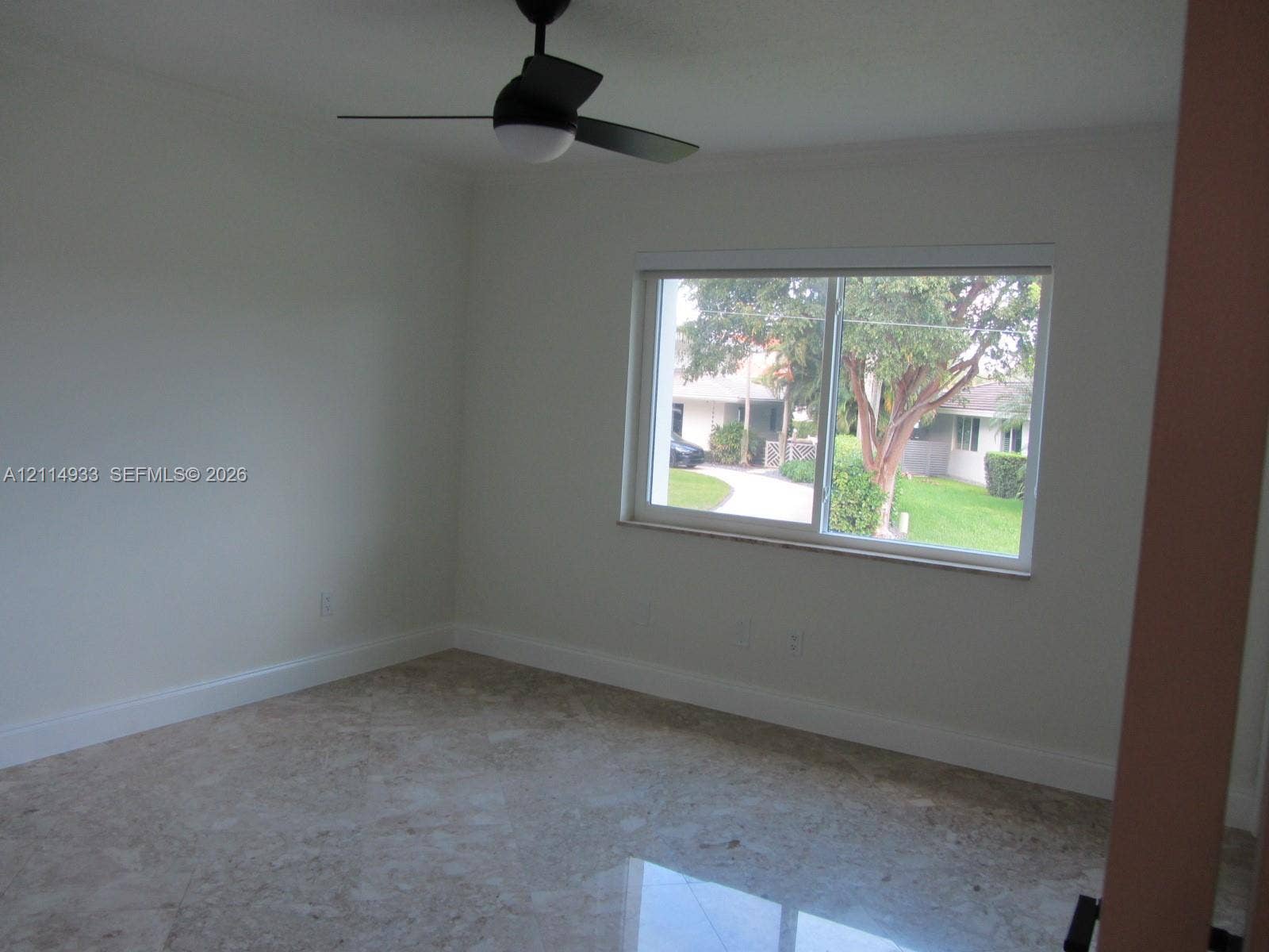 1001 Bella Vista Avenue, Coral Gables, Coral Gables, FL 33156 Neutral-toned interior space featuring light-colored stone-finish flooring, a matte black ceiling fan with integrated lighting, and a large horizontal sliding window