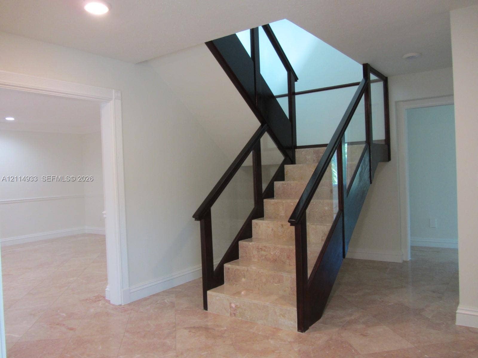 1001 Bella Vista Avenue, Coral Gables, Coral Gables, FL 33156 Staircase featuring natural stone treads, dark wood handrails, and glass panel balustrades beneath a skylight
