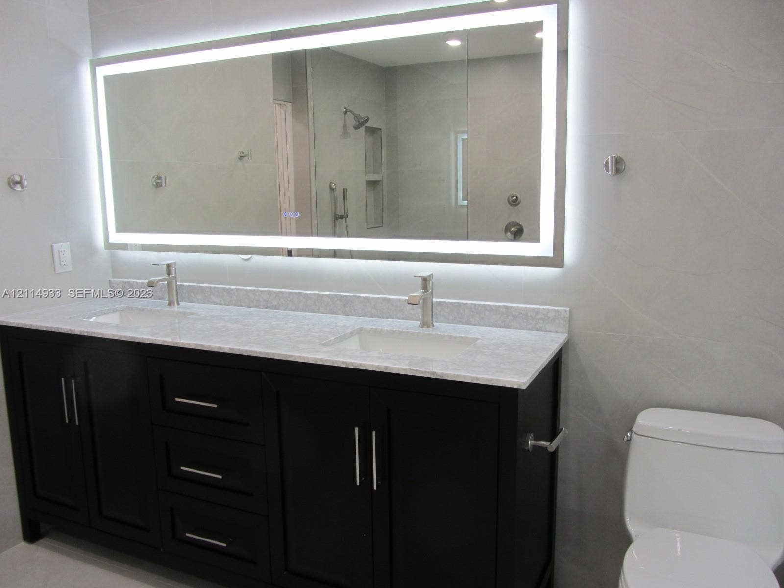 1001 Bella Vista Avenue, Coral Gables, Coral Gables, FL 33156 Dual-sink vanity featuring a stone countertop, oversized LED-backlit mirror, dark-finish cabinetry, and chrome-finish faucets