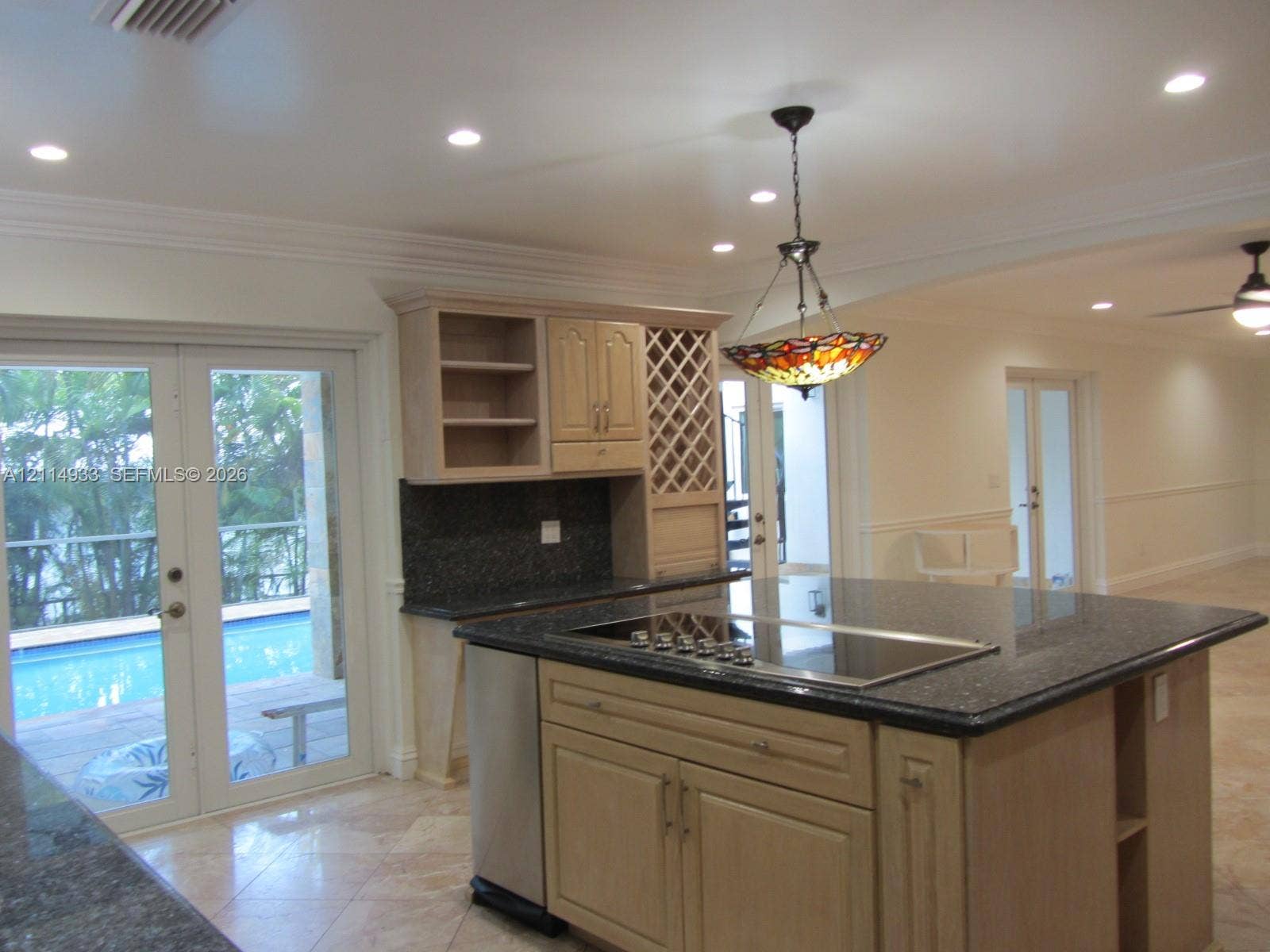 1001 Bella Vista Avenue, Coral Gables, Coral Gables, FL 33156 Kitchen featuring an expansive center island with a built-in cooktop, stone-finish countertops, custom wood cabinetry with integrated wine storage, and stone flooring throughout