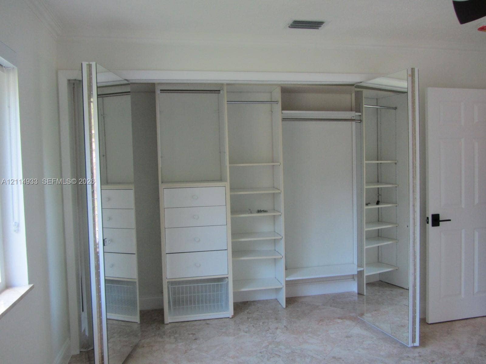 1001 Bella Vista Avenue, Coral Gables, Coral Gables, FL 33156 Custom reach-in closet featuring mirrored bi-fold doors, integrated shelving, multi-level hanging rods, and built-in drawer storage
