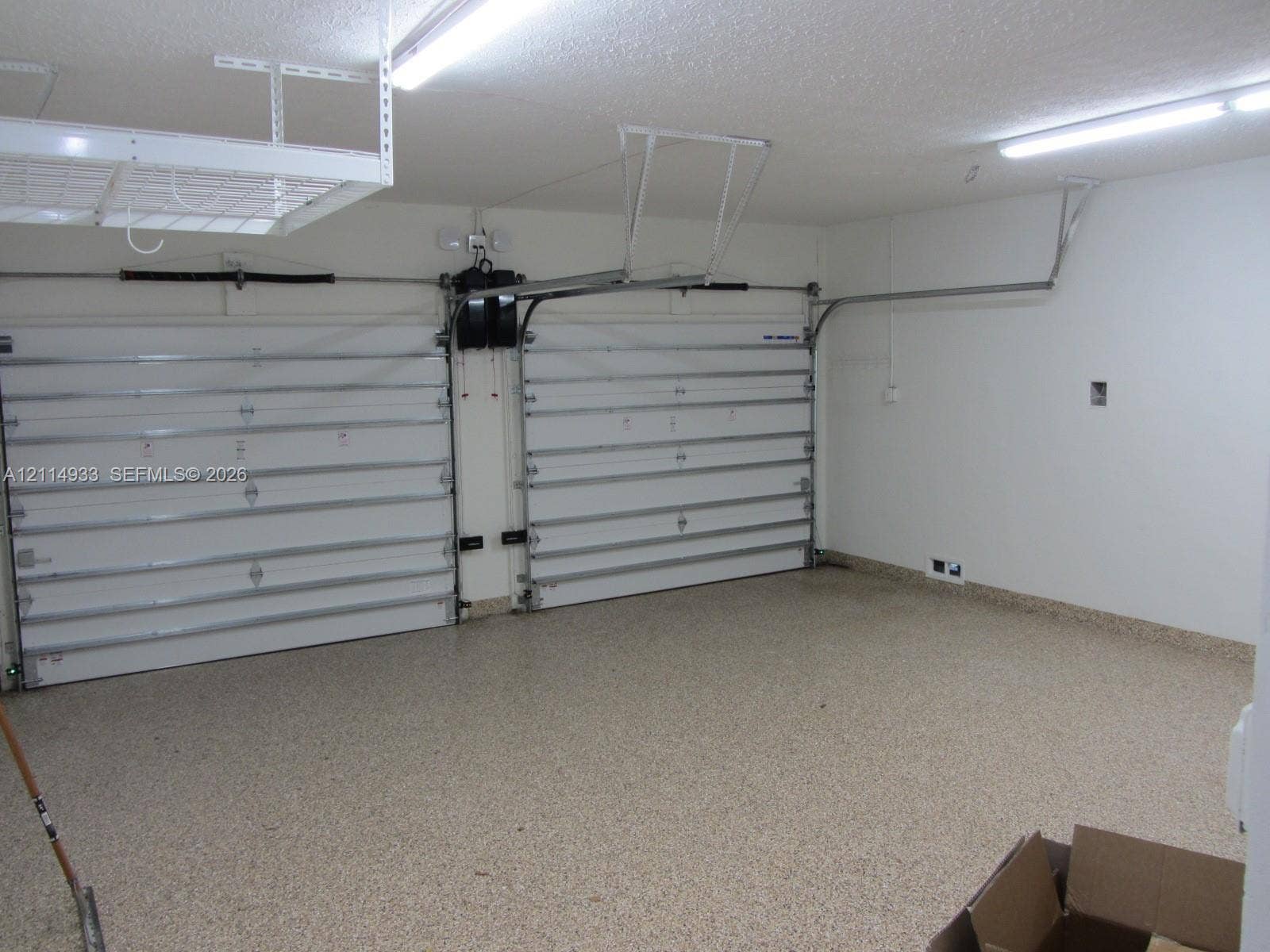 1001 Bella Vista Avenue, Coral Gables, Coral Gables, FL 33156 Two-car garage featuring dual overhead doors, overhead storage shelving, interior LED lighting, and speckled epoxy flooring