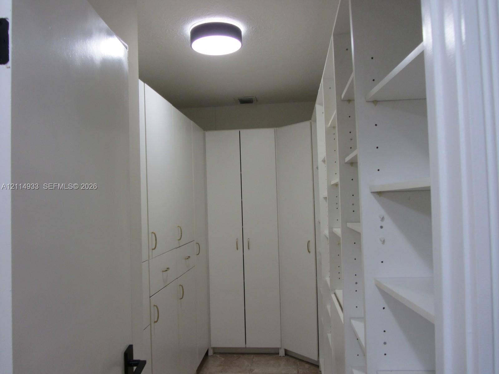 1001 Bella Vista Avenue, Coral Gables, Coral Gables, FL 33156 Custom floor-to-ceiling cabinetry featuring white laminate finish, adjustable shelving, integrated storage drawers, gold-toned hardware, and a circular flush-mount ceiling light