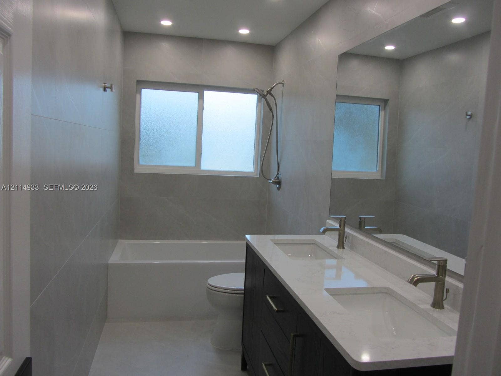 1001 Bella Vista Avenue, Coral Gables, Coral Gables, FL 33156 Dual-sink vanity with a quartz countertop, full-width wall mirror, recessed ceiling lighting, and large-format tile wall surround with a built-in tub