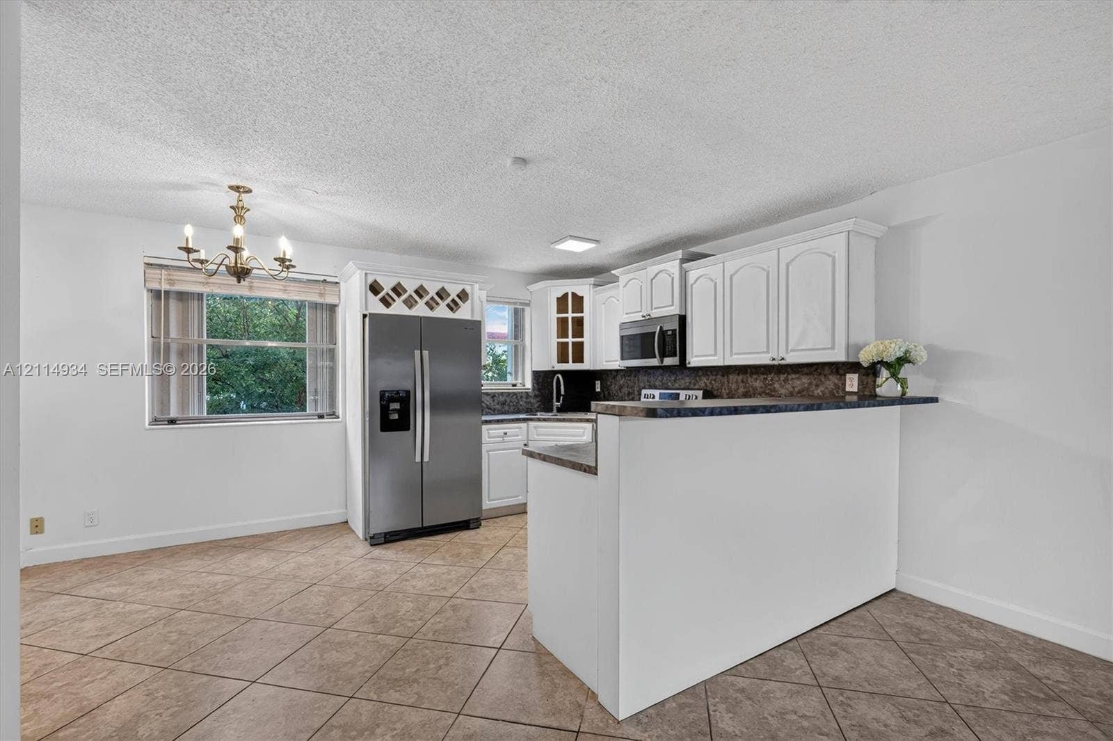 Kitchen featuring white shaker-style cabinetry, stainless steel appliances, a built-in wine rack, stone-finish countertops, and tile flooring