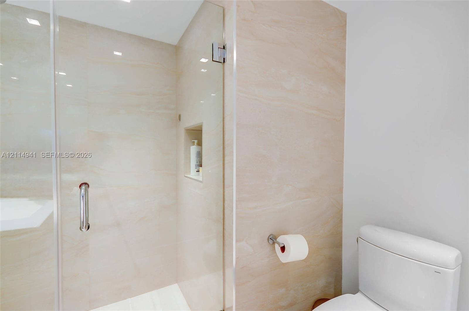 16175 Golf Club Road, #113, Weston, FL 33326 Walk-in shower featuring large-format stone-look tile, frameless glass door, polished chrome hardware, and built-in recessed wall niche
