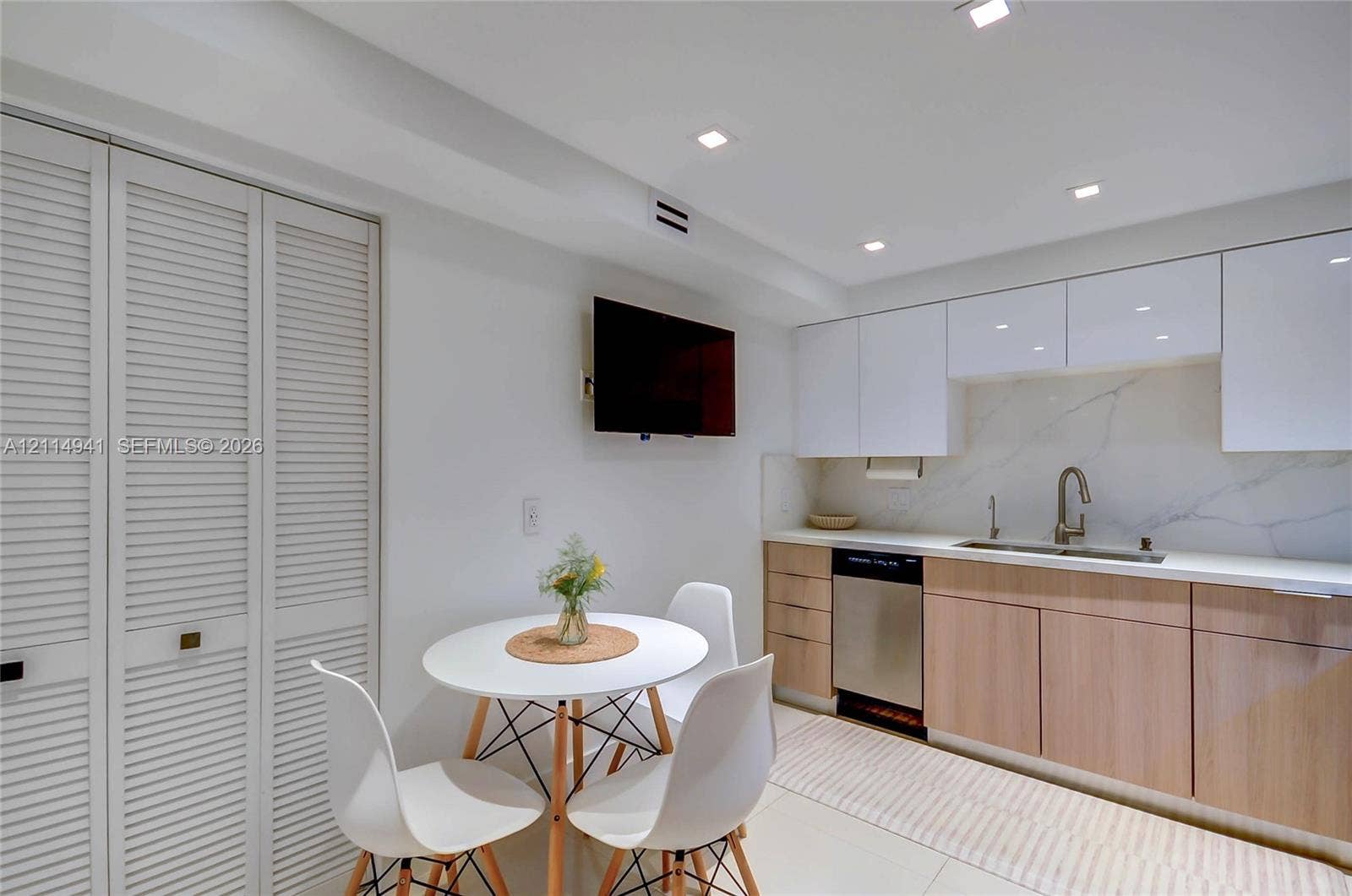 16175 Golf Club Road, #113, Weston, FL 33326 Kitchen area featuring high-gloss white upper cabinetry, wood-finish lower cabinetry, stone-style slab backsplash, recessed ceiling lighting, and floor-to-ceiling louvered closet doors