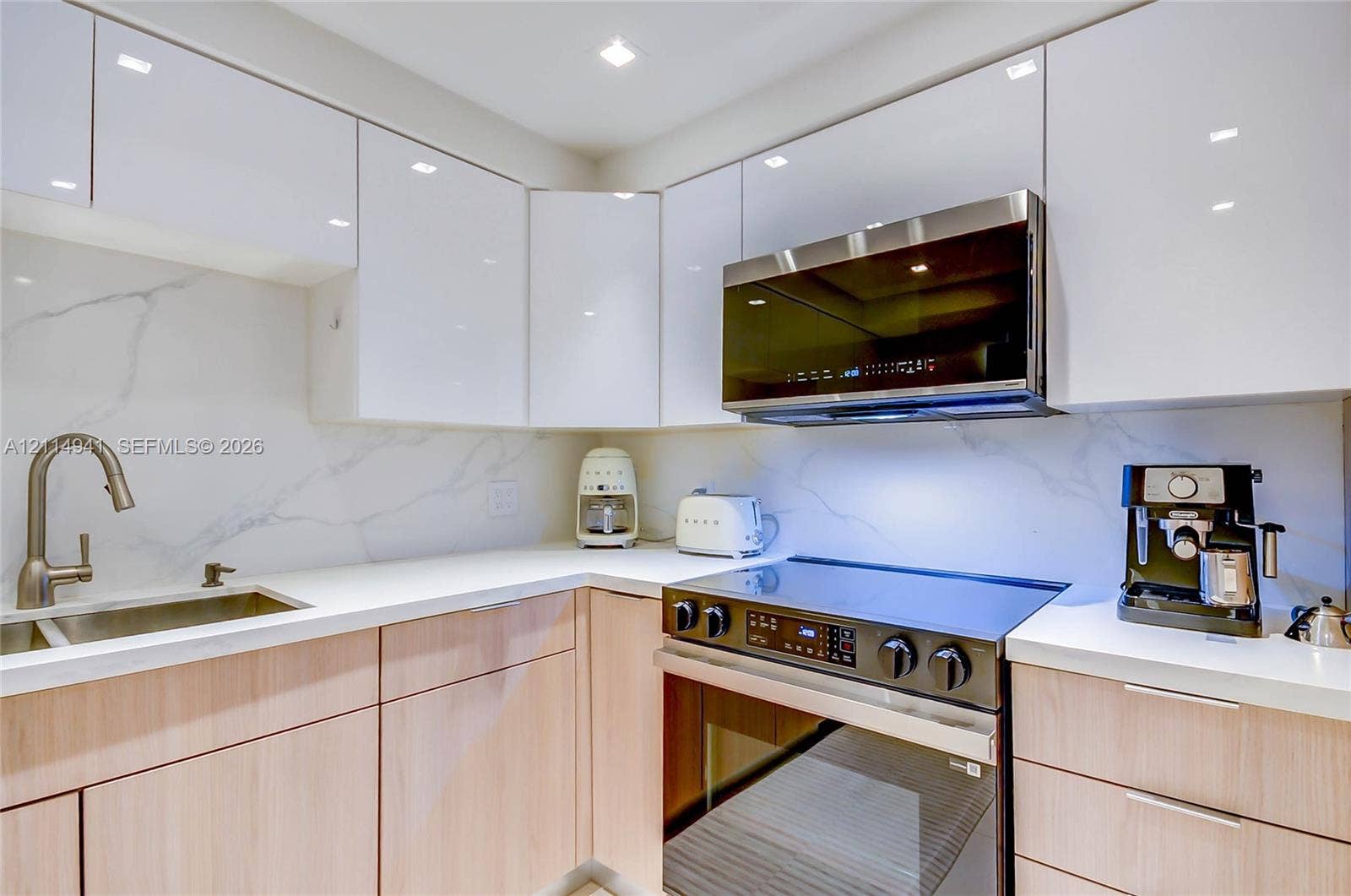 16175 Golf Club Road, #113, Weston, FL 33326 Modern kitchen featuring high-gloss white upper cabinetry, wood-finish lower cabinetry, solid-surface countertops, stone-patterned backsplash, and integrated stainless steel appliances