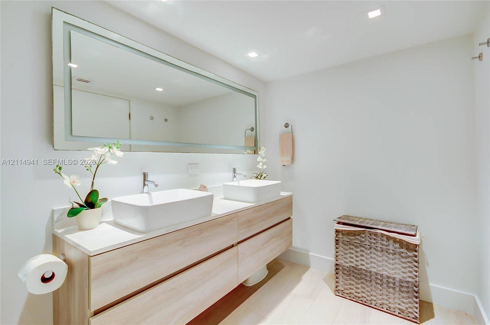16175 Golf Club Road, #113, Weston, FL 33326 Floating dual-vanity cabinet with light wood-finish cabinetry, white countertop, rectangular vessel sinks, and an oversized illuminated wall mirror with integrated lighting