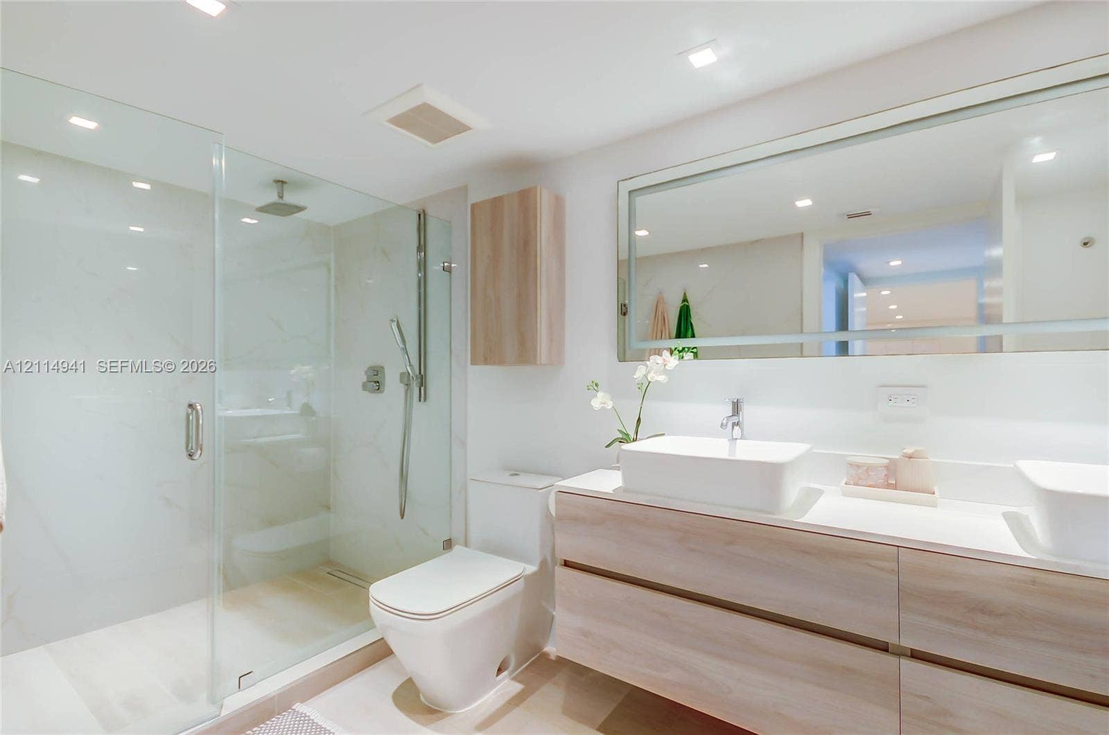 16175 Golf Club Road, #113, Weston, FL 33326 Bathroom featuring a floating wood-finish double vanity, dual vessel sinks, glass-enclosed shower with tiled walls, and an expansive wall-mounted mirror