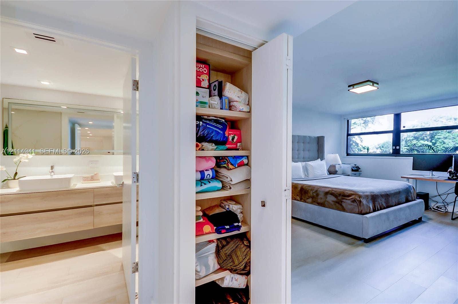 16175 Golf Club Road, #113, Weston, FL 33326 Built-in floor-to-ceiling storage cabinetry with adjustable shelving, light wood-finish floating vanity with dual rectangular vessel sinks, expansive vanity mirror, and large-format window panels