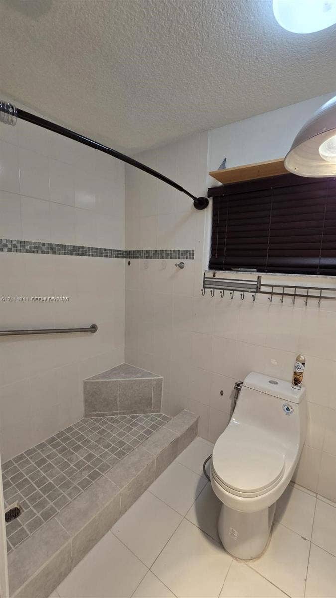 Walk-in shower featuring a built-in corner bench, mosaic tile flooring, decorative tile inlay, and white wall tiling with a stainless steel grab bar