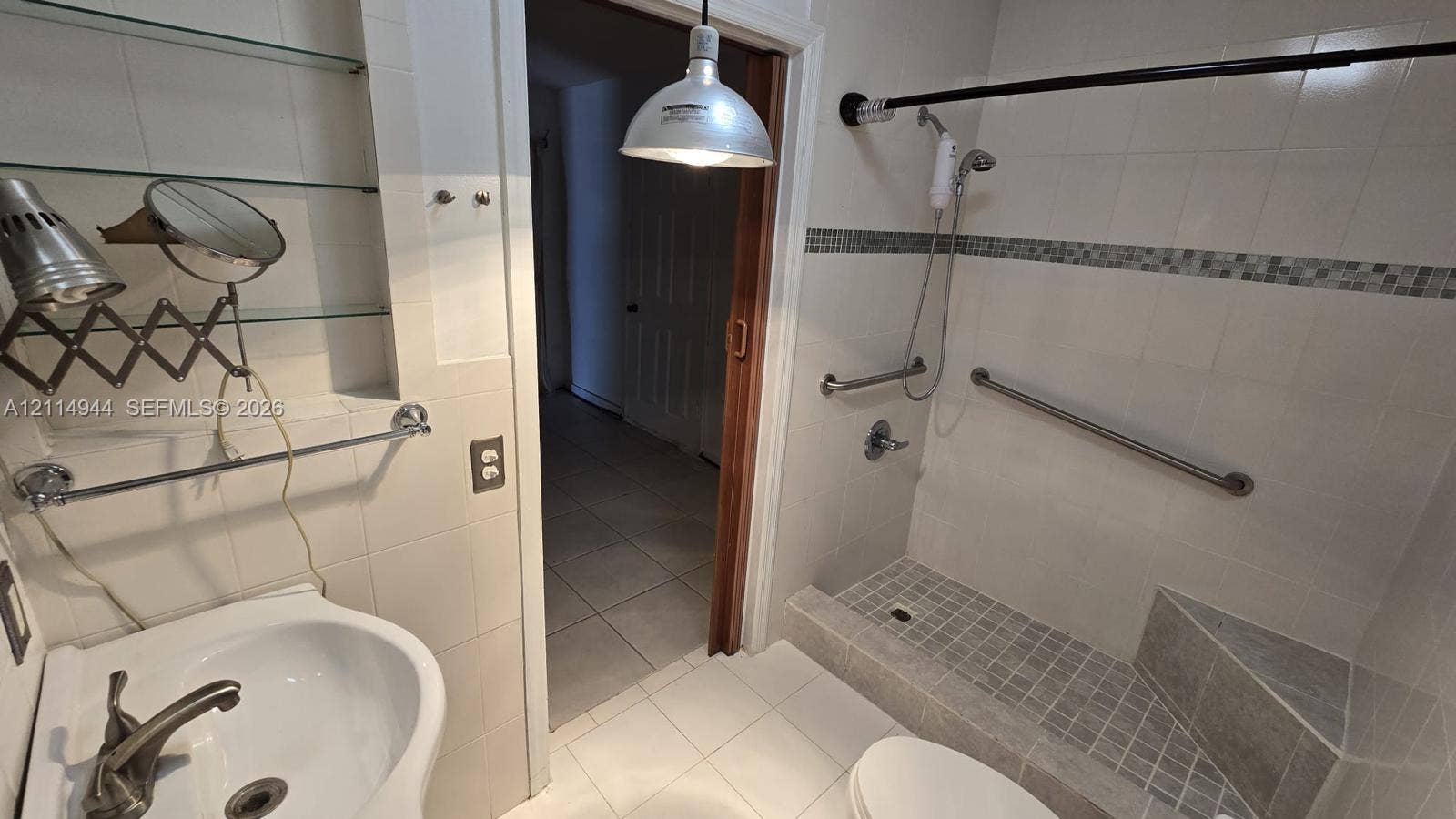 Bathroom featuring tiled flooring and walls, a step-in shower with integrated corner seating, wall-mounted metal grab bars, and a pendant-style light fixture