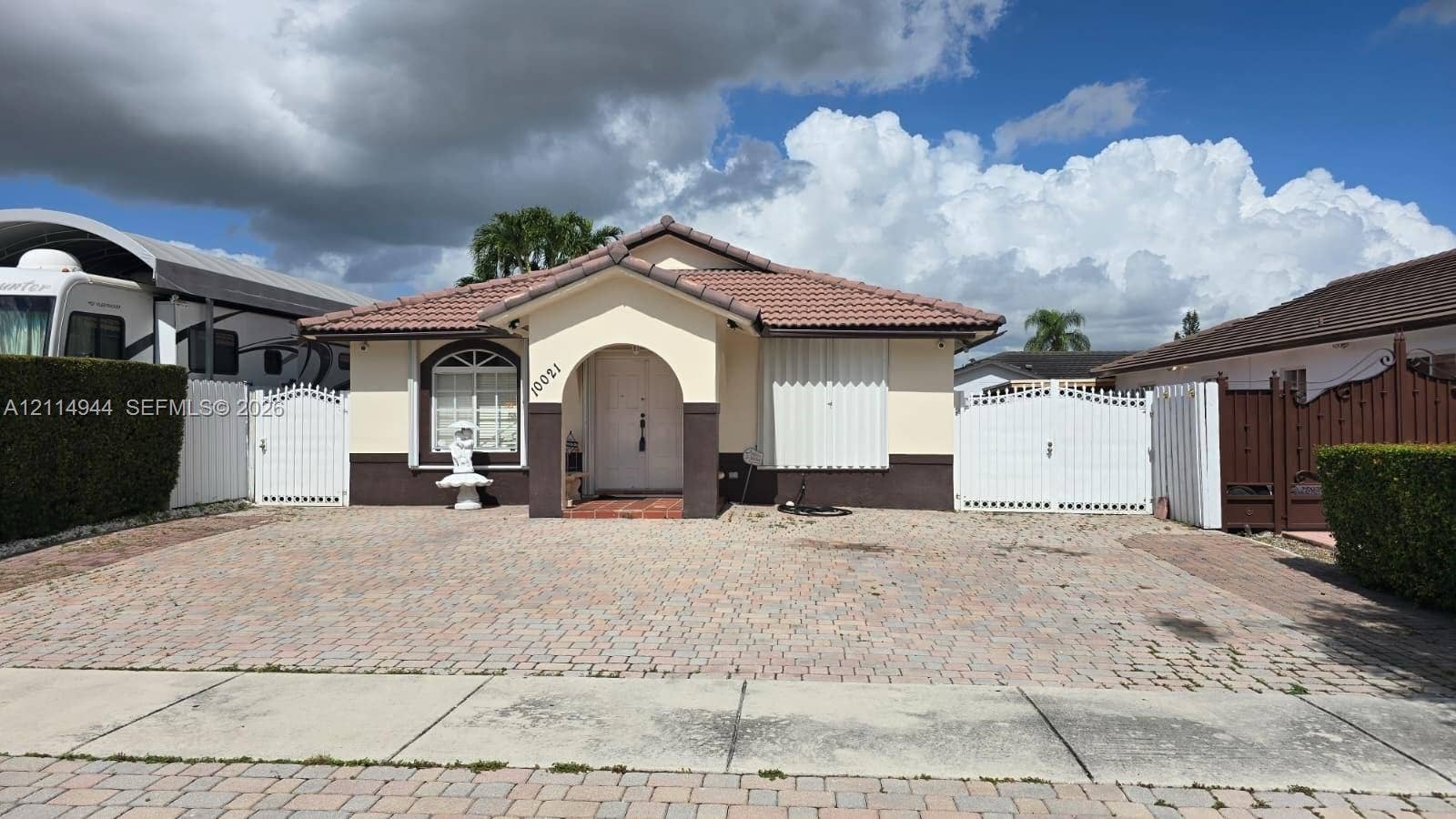 Single-story exterior featuring a tile roof, arched entryway, paved driveway, and dual white gate enclosures