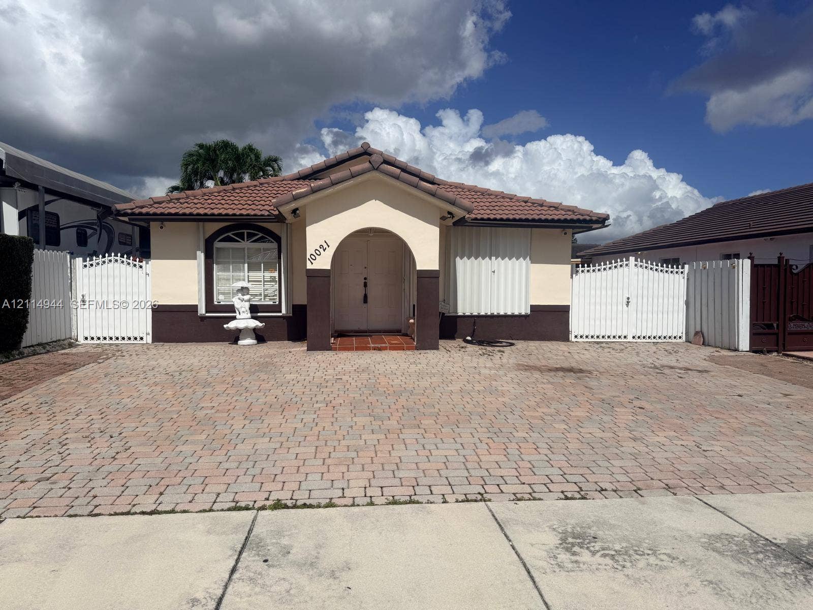 Single-story residence featuring a tile roof, paver driveway, arched entryway, and dual white privacy gates