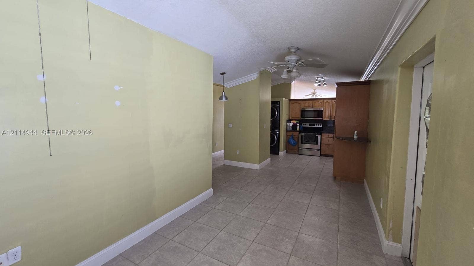 Interior space featuring neutral floor tiling, crown molding, ceiling-mounted light fixtures, and cabinetry with integrated stainless steel appliances