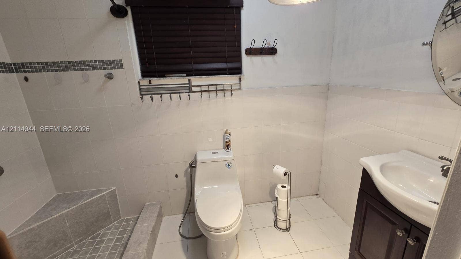 Bathroom featuring white wall tiling with a mosaic accent border, a walk-in tiled shower with a built-in bench, and a dark wood vanity with a white integrated sink