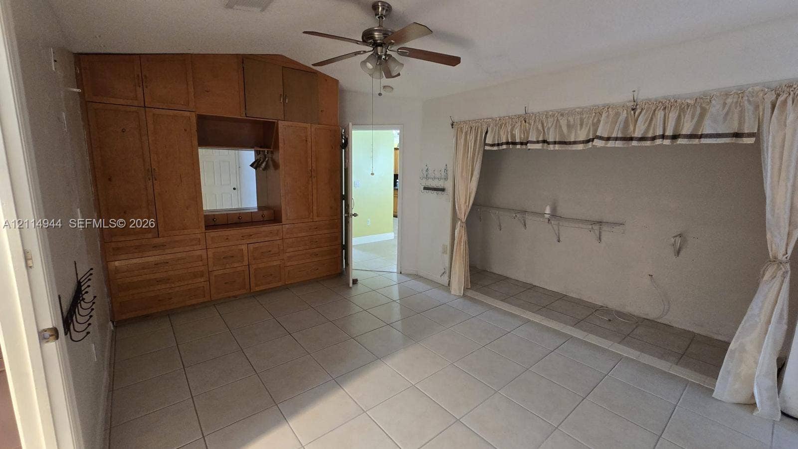 Room featuring light-colored tile flooring, floor-to-ceiling wooden built-in cabinetry, and a ceiling fan with integrated lighting