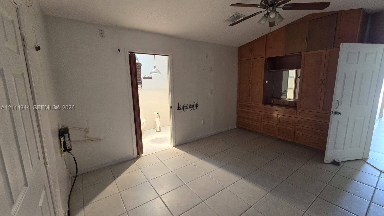 Vaulted ceiling with a central paddle fan, extensive built-in wood-finish cabinetry, and large-format tile flooring