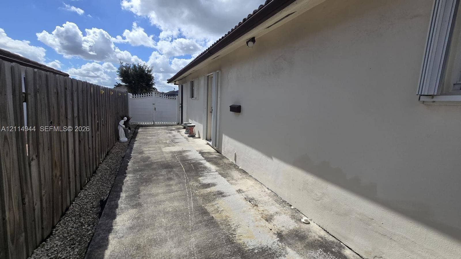 Exterior side yard featuring a concrete pathway, perimeter wood fencing, and a white privacy gate