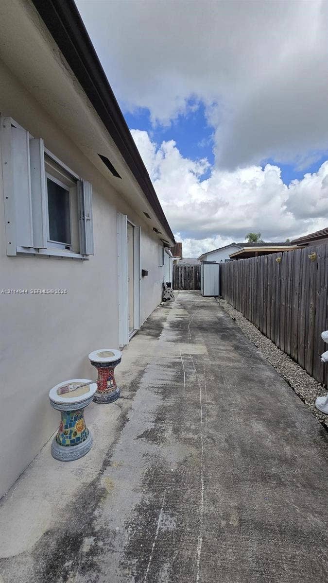 Side exterior featuring a concrete walkway, smooth stucco siding, and a wood privacy fence