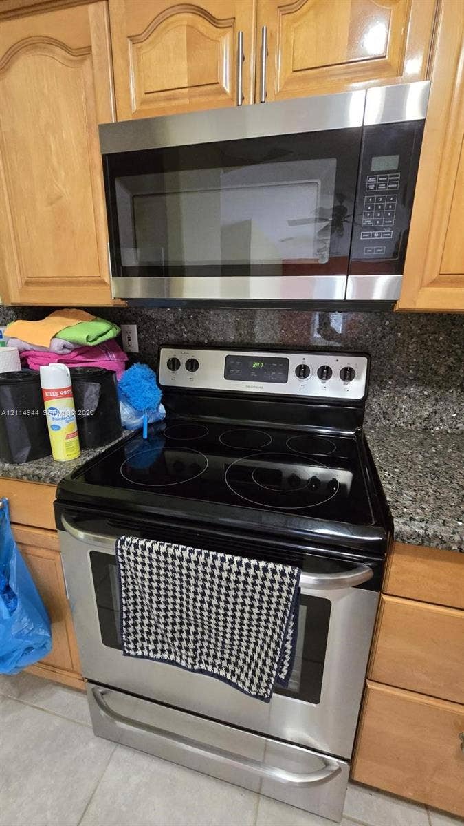 Stainless steel electric range with smooth-top cooktop, matching over-the-range microwave, stone-finish countertops, and wood-finish cabinetry