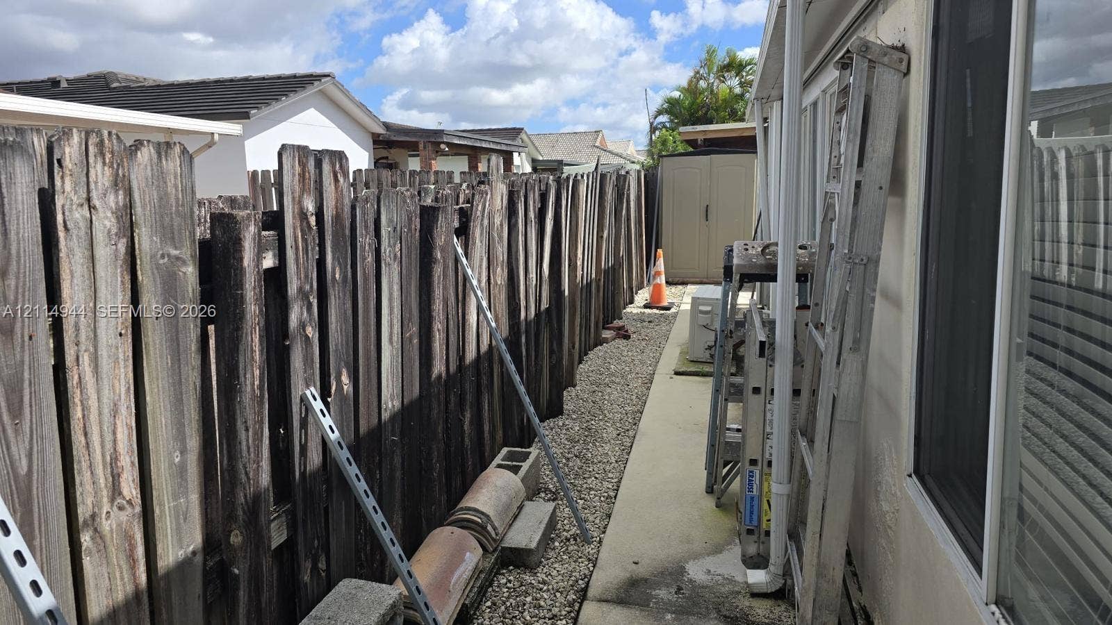 Concrete side walkway featuring a perimeter wood fence, gravel ground cover, and exterior sliding glass door