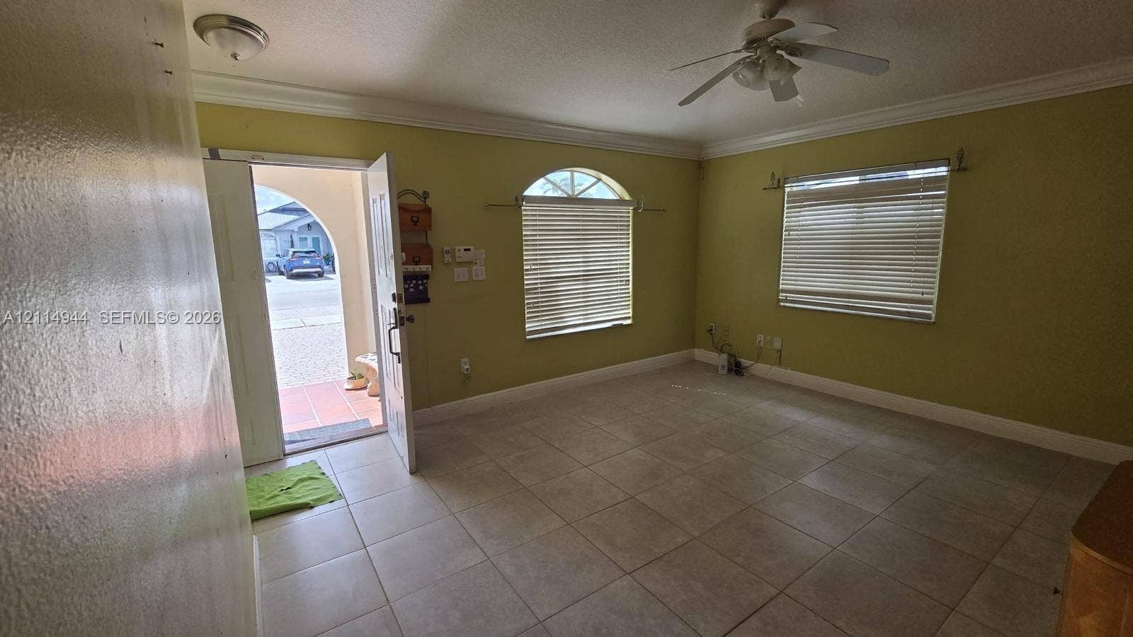 Neutral-toned ceramic tile flooring, arched window with horizontal blinds, ceiling fan with integrated lighting, and white door frame with crown molding