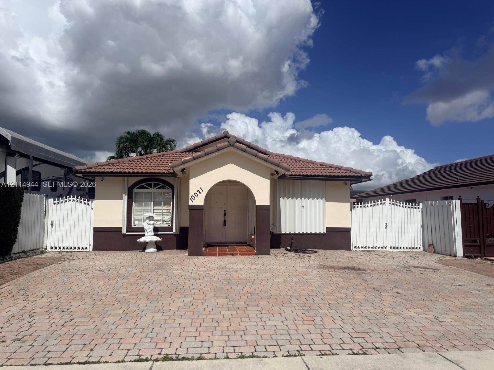 Single-story residence featuring a terracotta-tiled roof, arched entryway, paved driveway, and decorative metal perimeter gates