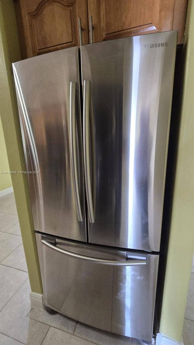 Stainless steel French door refrigerator with bottom-mount freezer, paired with wood-finish cabinetry and tile flooring