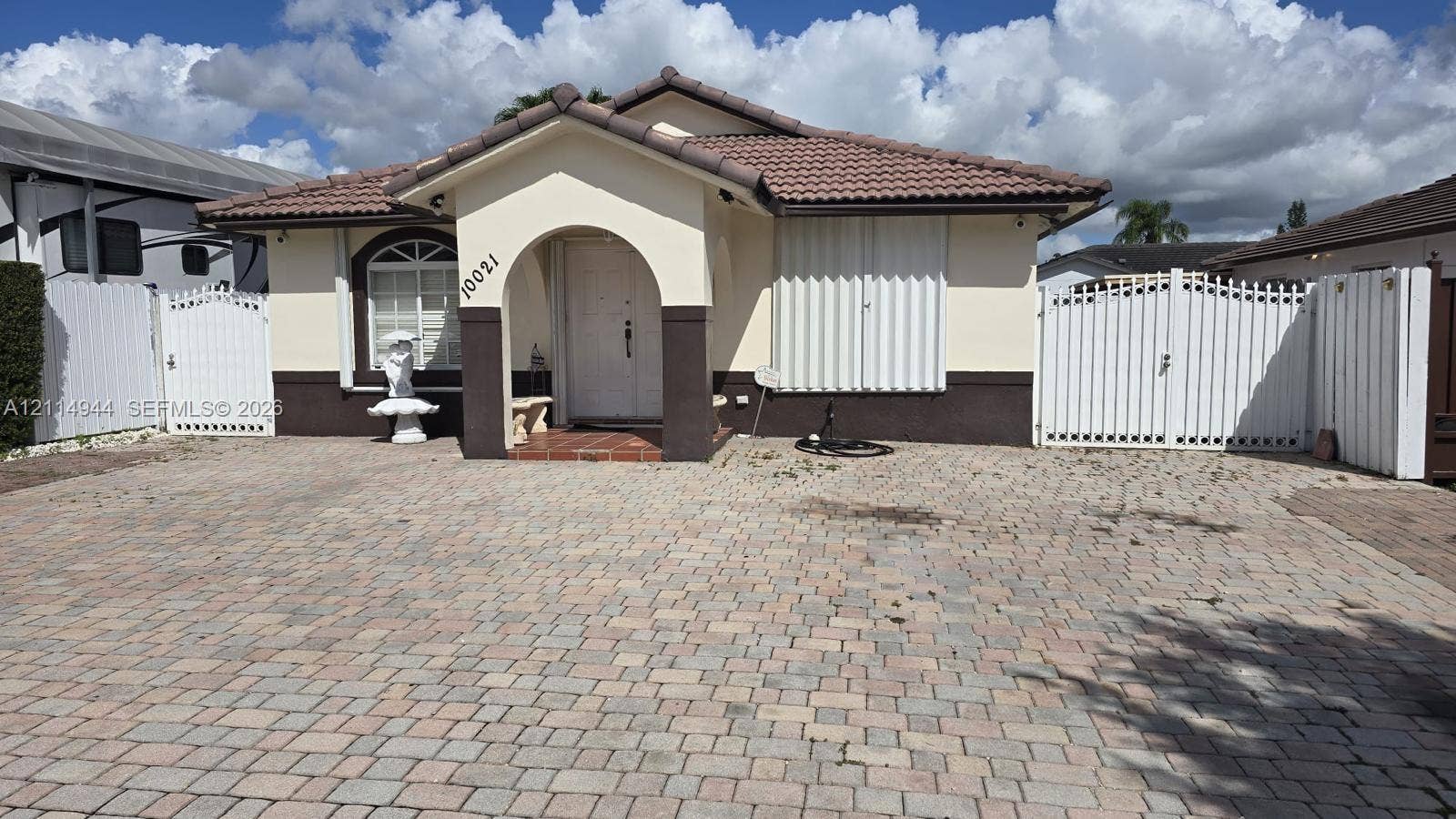 Single-story residence featuring a paved brick driveway, tile roof, arched entryway, and dual side-yard gates