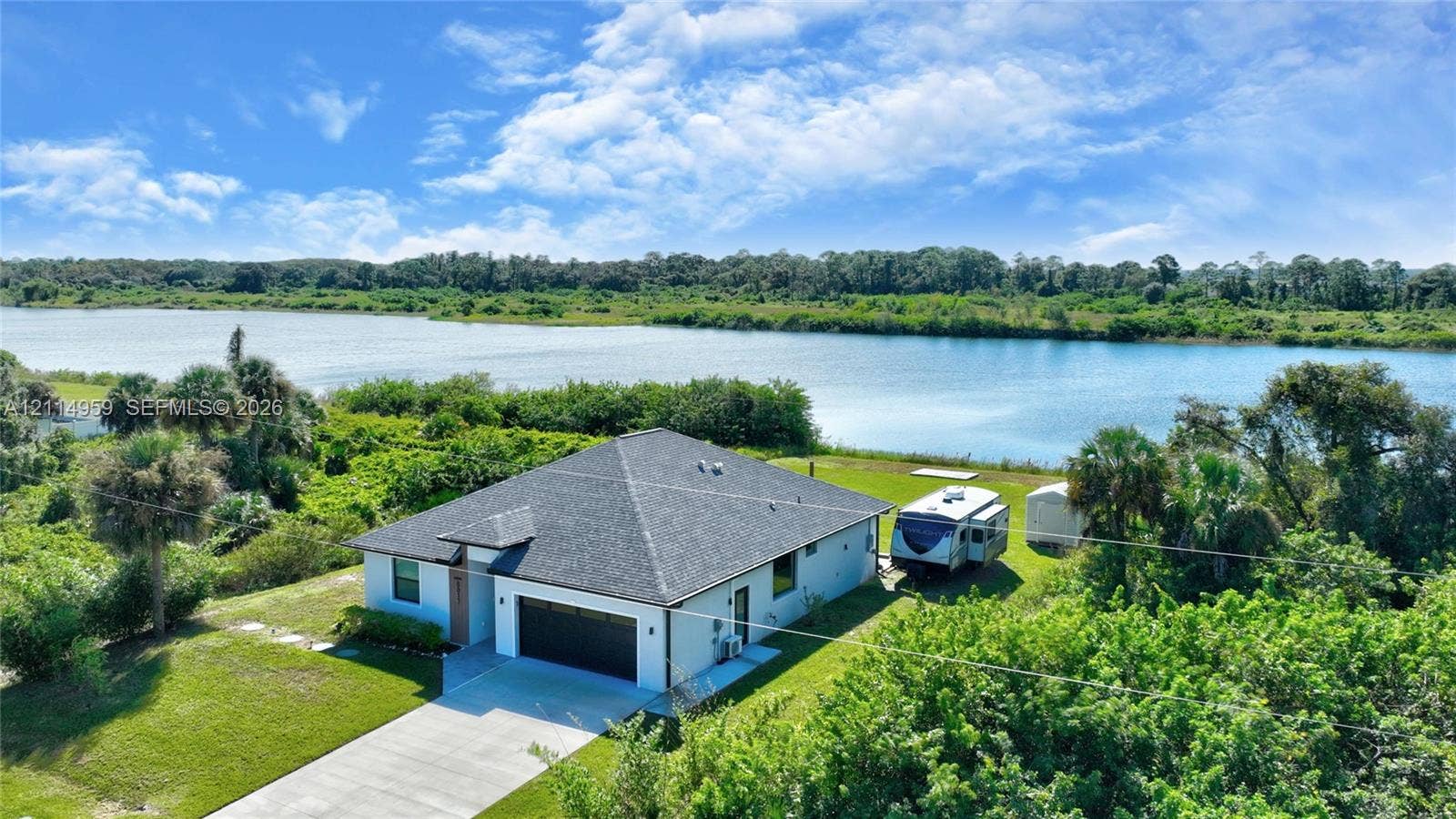 8017 Sunrise Circle, Labelle, FL 33935 Single-story residence featuring a dark shingle roof, attached two-car garage, concrete driveway, and direct waterfront positioning