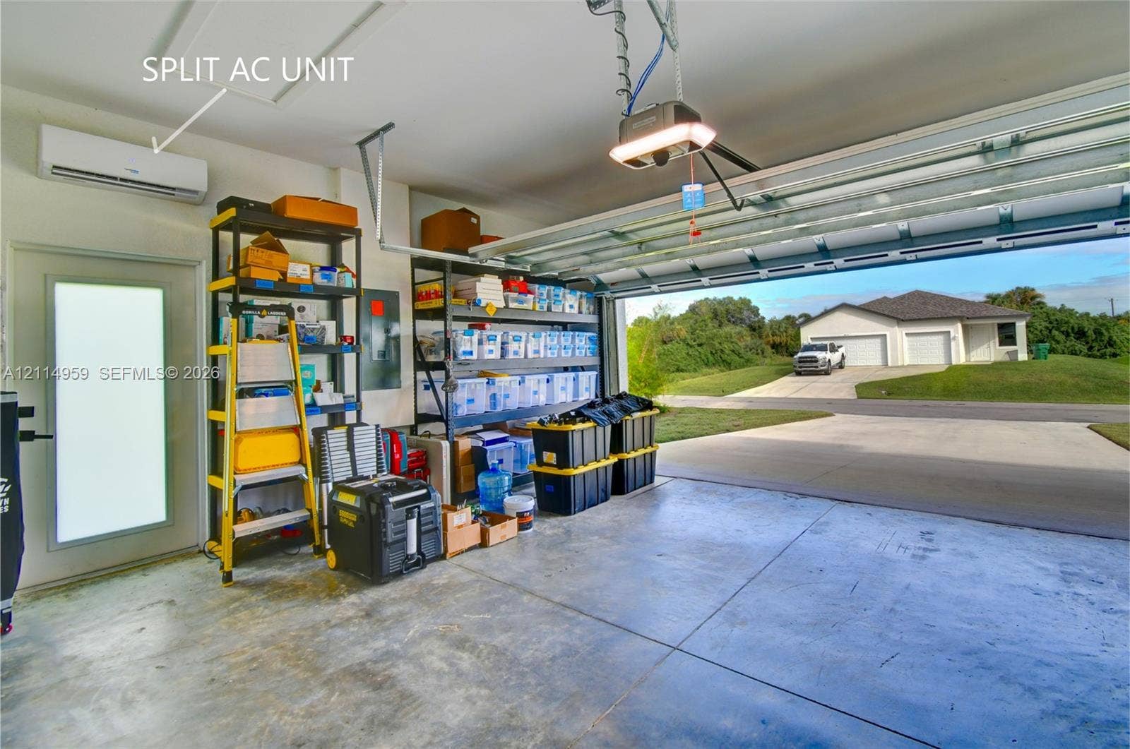 8017 Sunrise Circle, Labelle, FL 33935 Attached garage featuring concrete flooring, a wall-mounted split-system air conditioning unit, automated garage door opener, and a frosted-glass panel door