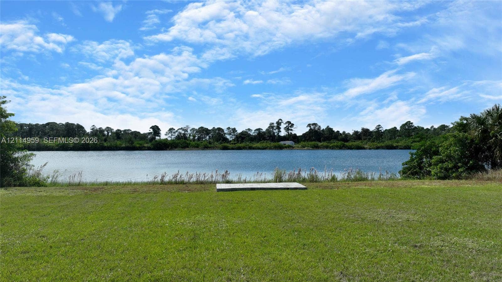 8017 Sunrise Circle, Labelle, FL 33935 Waterfront lot featuring a manicured lawn, a concrete pad, and mature perimeter trees
