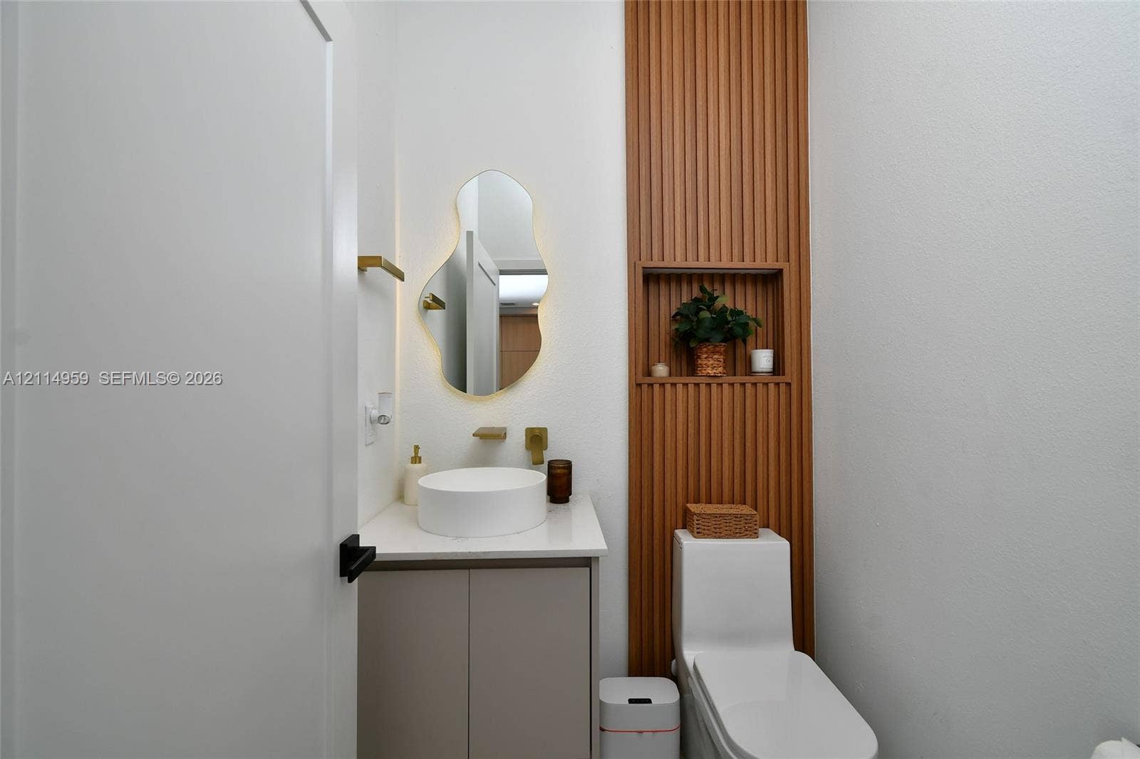 8017 Sunrise Circle, Labelle, FL 33935 Custom vanity with a solid surface countertop and circular vessel sink, wall-mounted metallic faucet, asymmetrical backlit mirror, and vertical wood-slat accent wall featuring a recessed built-in niche