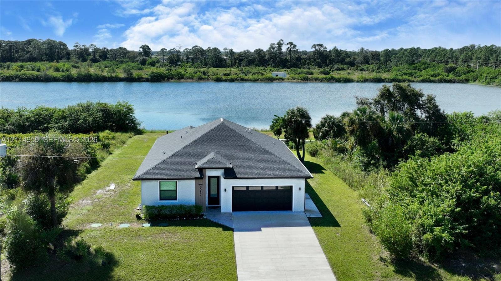 8017 Sunrise Circle, Labelle, FL 33935 Single-story exterior featuring a concrete driveway, two-car garage with modern paneling, hip roofline, and waterfront positioning