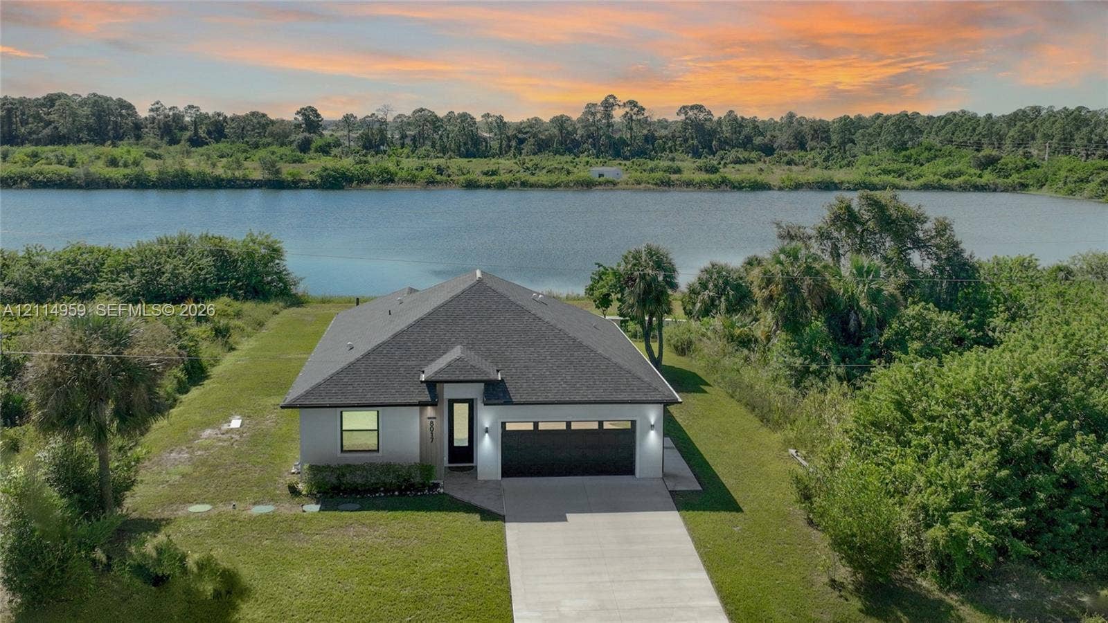 8017 Sunrise Circle, Labelle, FL 33935 Single-story residence featuring a dark shingled roof, stucco exterior, concrete driveway, attached multi-car garage, and waterfront positioning