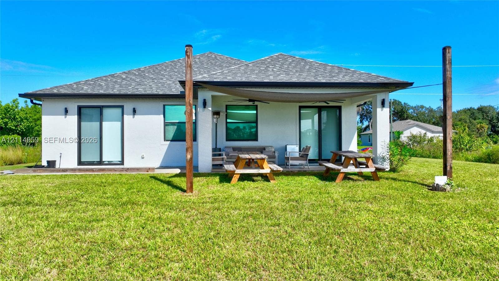 8017 Sunrise Circle, Labelle, FL 33935 Rear exterior featuring a covered patio, dual sliding glass door entries, shingle roof, and expansive lawn