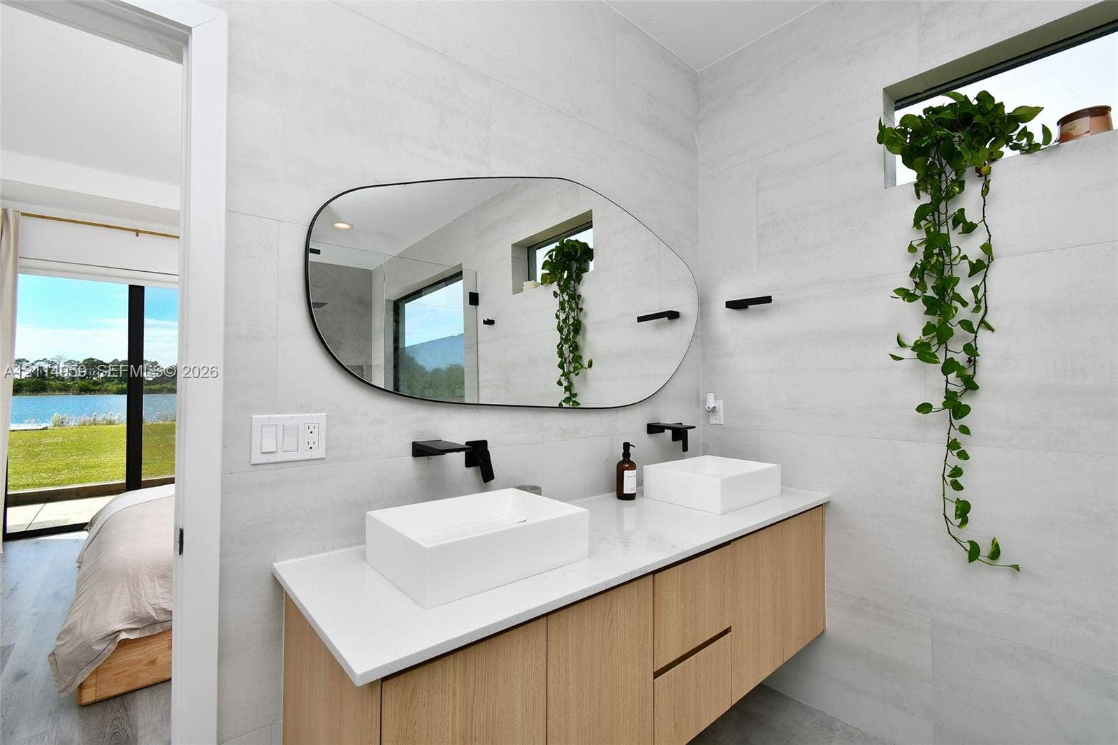 8017 Sunrise Circle, Labelle, FL 33935 Floating wood-finish vanity with a white countertop and dual rectangular vessel sinks, complemented by matte black wall-mounted faucets and an asymmetrical vanity mirror