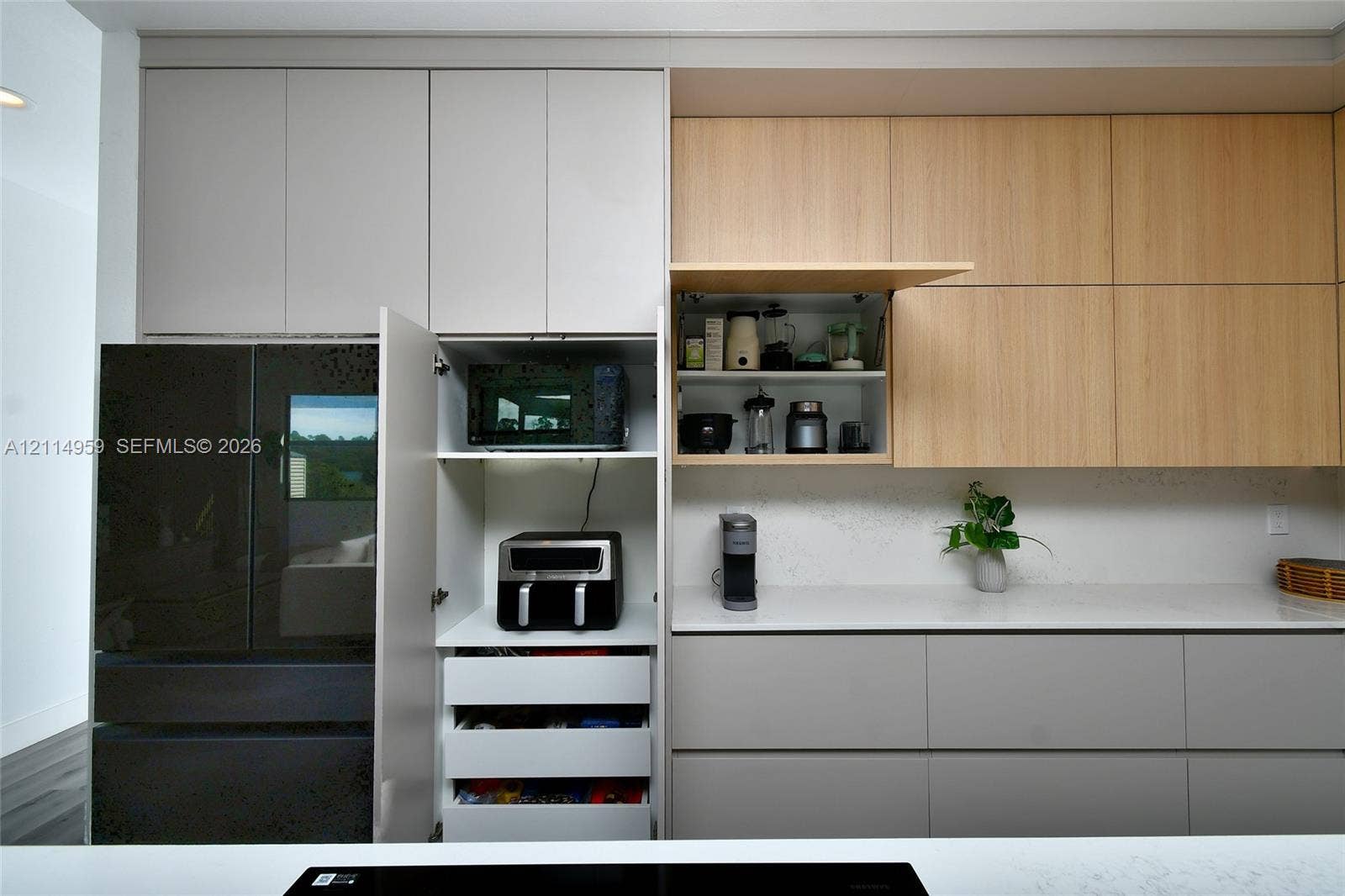 8017 Sunrise Circle, Labelle, FL 33935 Contemporary kitchen cabinetry featuring matte grey lower drawers, light wood-tone upper cabinets, integrated storage solutions, and white solid-surface countertops